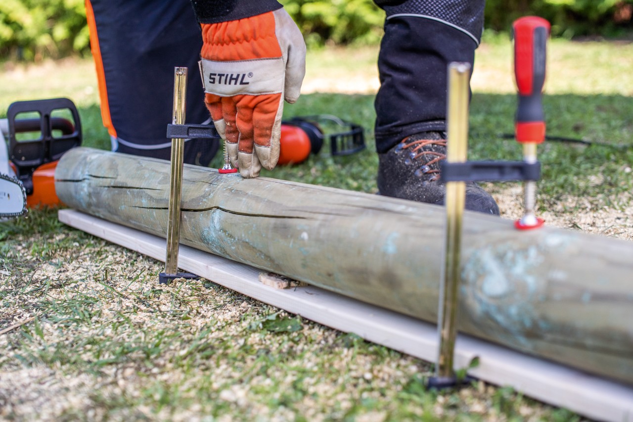 Un operario que sabe cómo construir un arenero para niños, fija un tronco con sargentos de apriete y unos guantes STIHL.