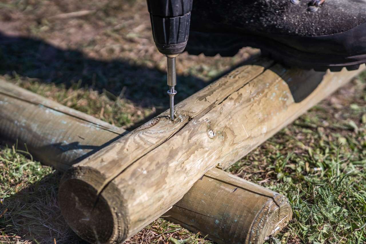 Un tornillo fija dos piezas de madera apiladas que se unen en una esquina para construir un arenero con STIHL.