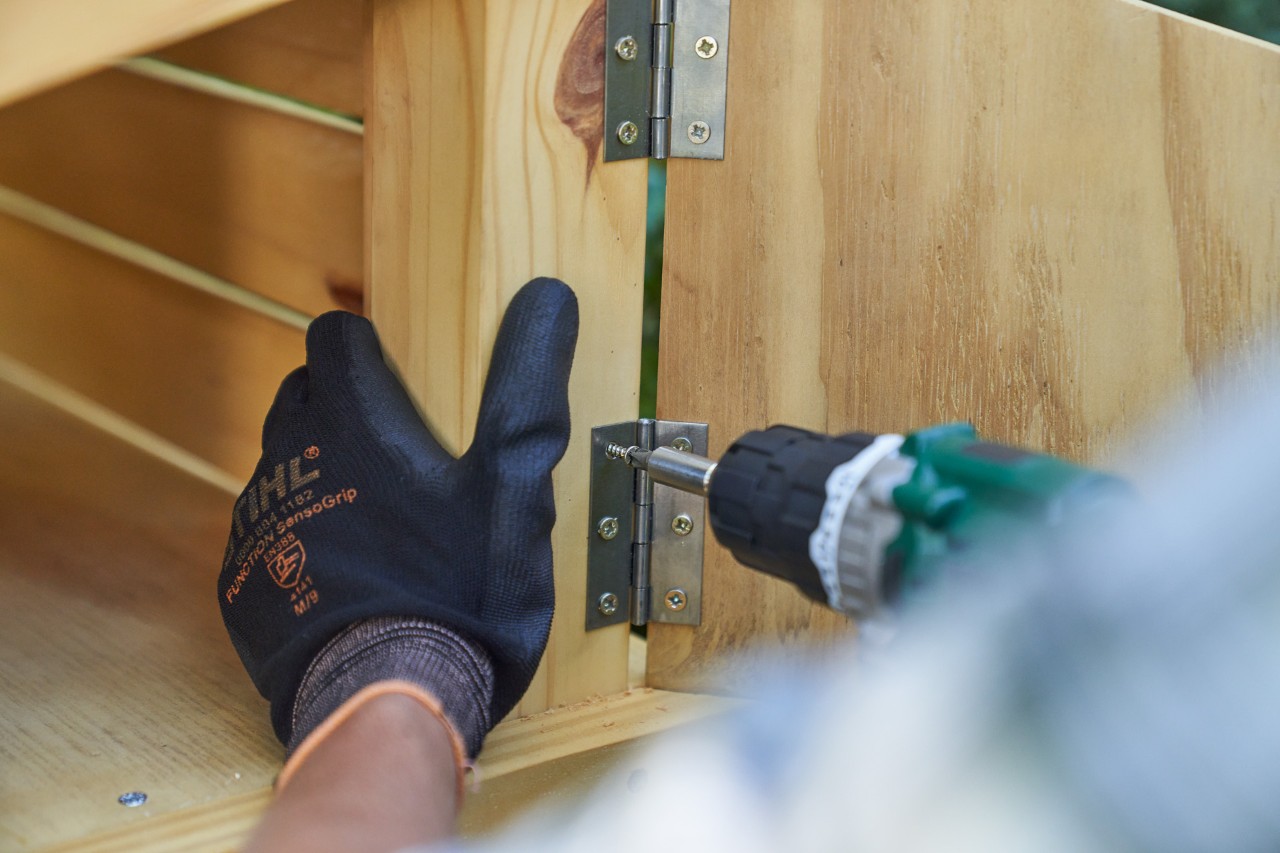 Una mano con el guante  STIHL FUNCTION SENSOTOUCH atornilla la puerta del compartimento portaobjetos del garaje 