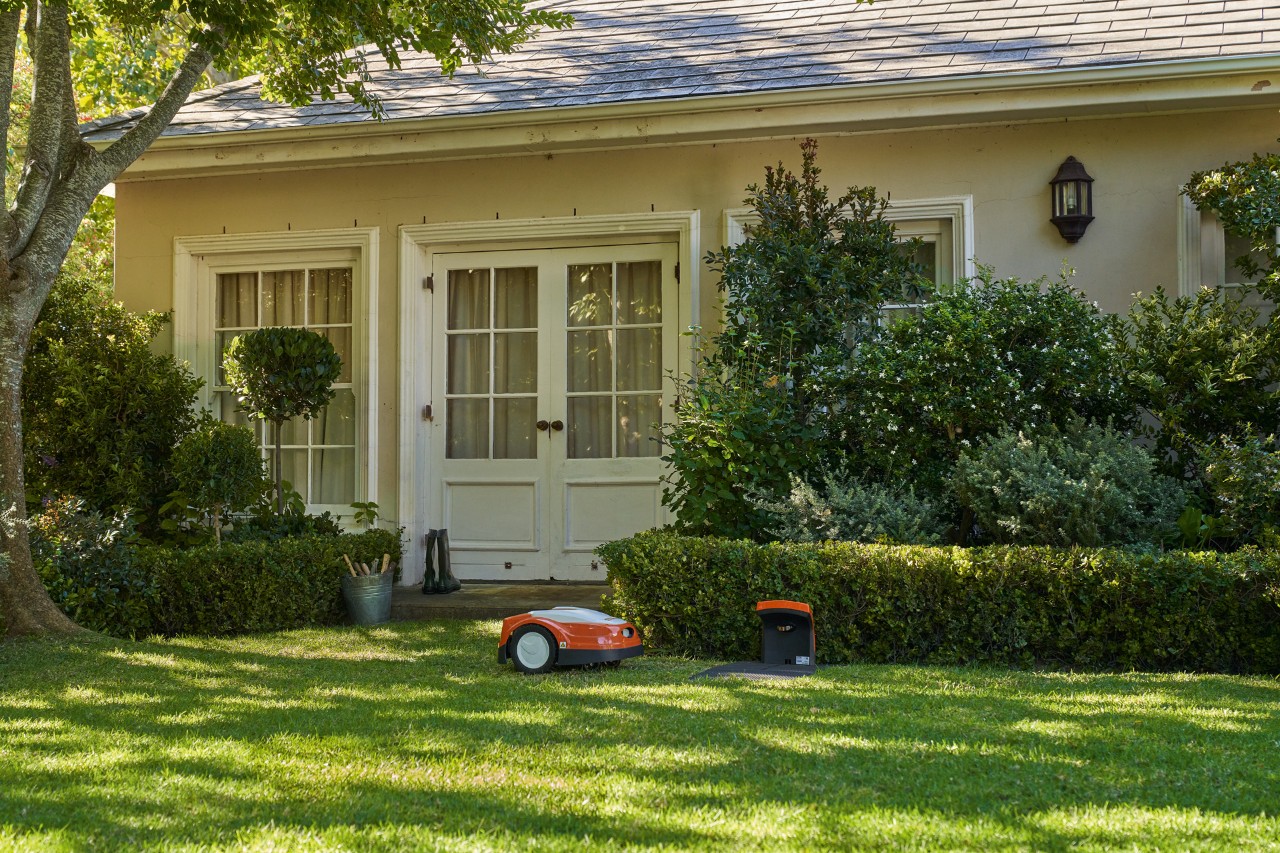 El robot cortacésped STIHL iMOW® se encuentra cerca de la estación de conexión sobre el césped verde de un jardín