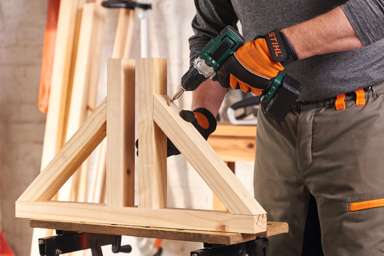 Persona con guantes de protección STIHL Function Protect atornilla los pies para una pantalla de privacidad de madera