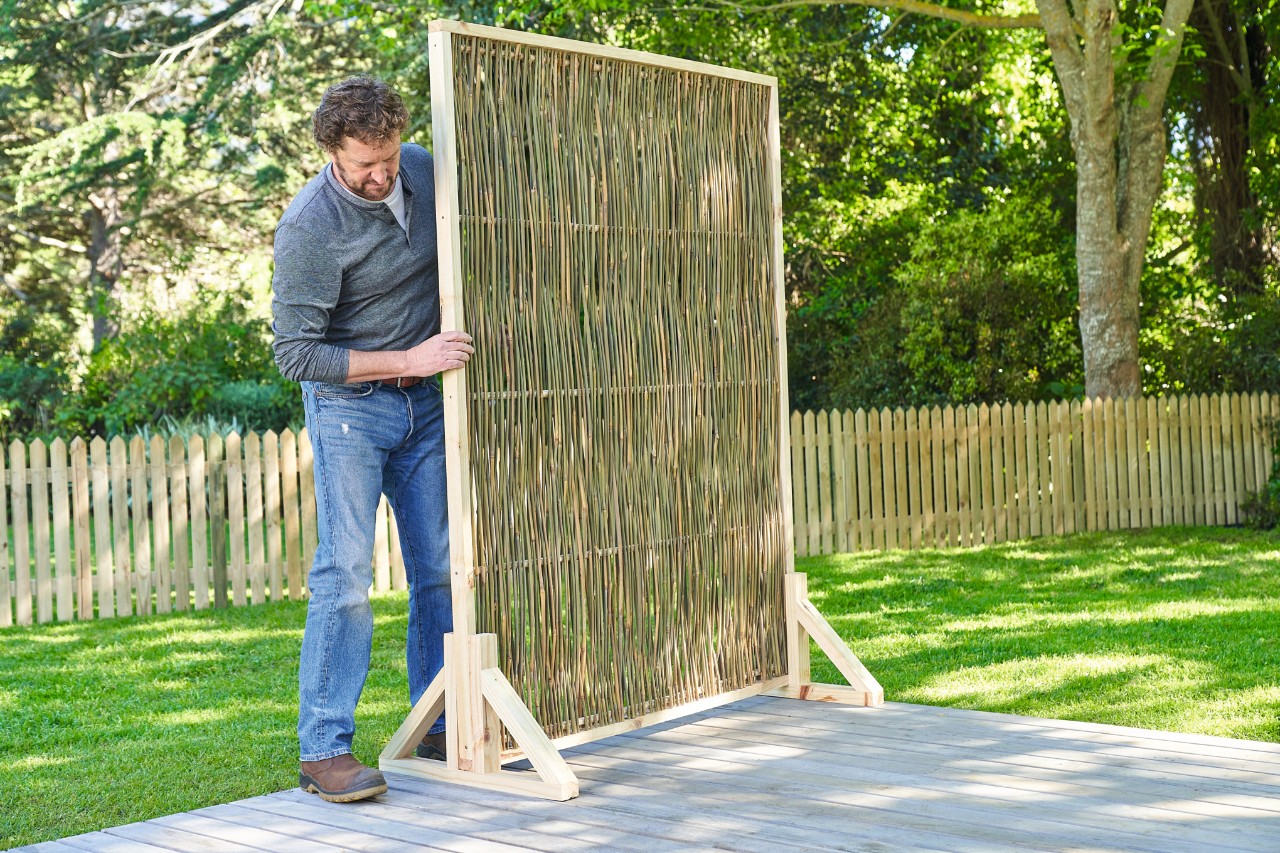 Un hombre coloca una pantalla de privacidad de madera de fabricación propia en tu terraza de madera