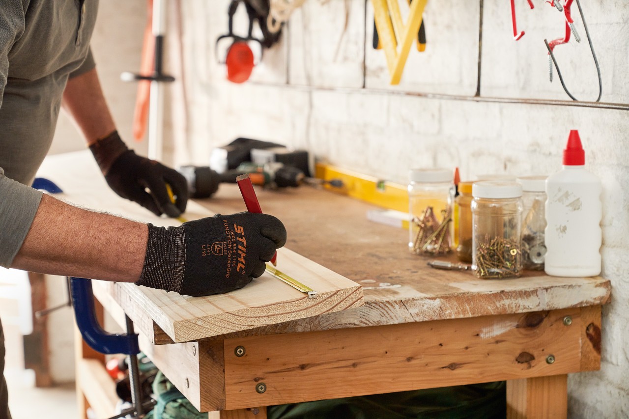 Un hombre con guantes de protección STIHL marca los orificios en una tabla de madera
