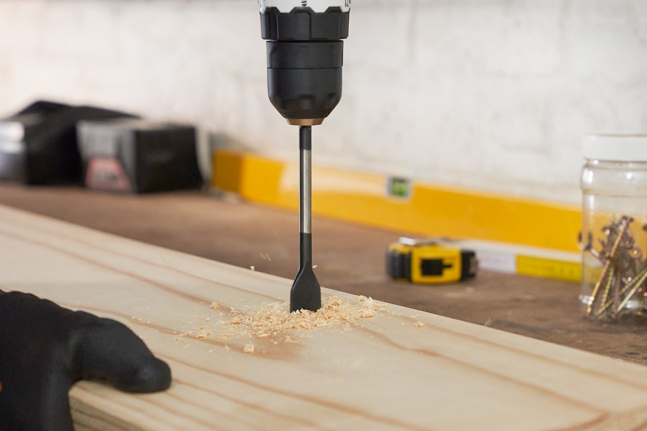 Una persona taladra agujeros en una tabla de madera para construir uno mismo un soporte para herramientas de jardín
