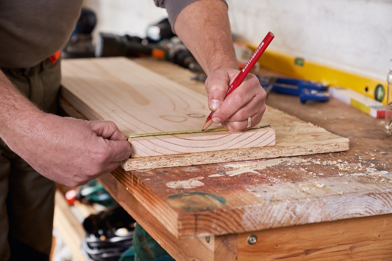 Un hombre marca los orificios en un tablero de madera para construir él mismo un soporte para máquinas de jardinería