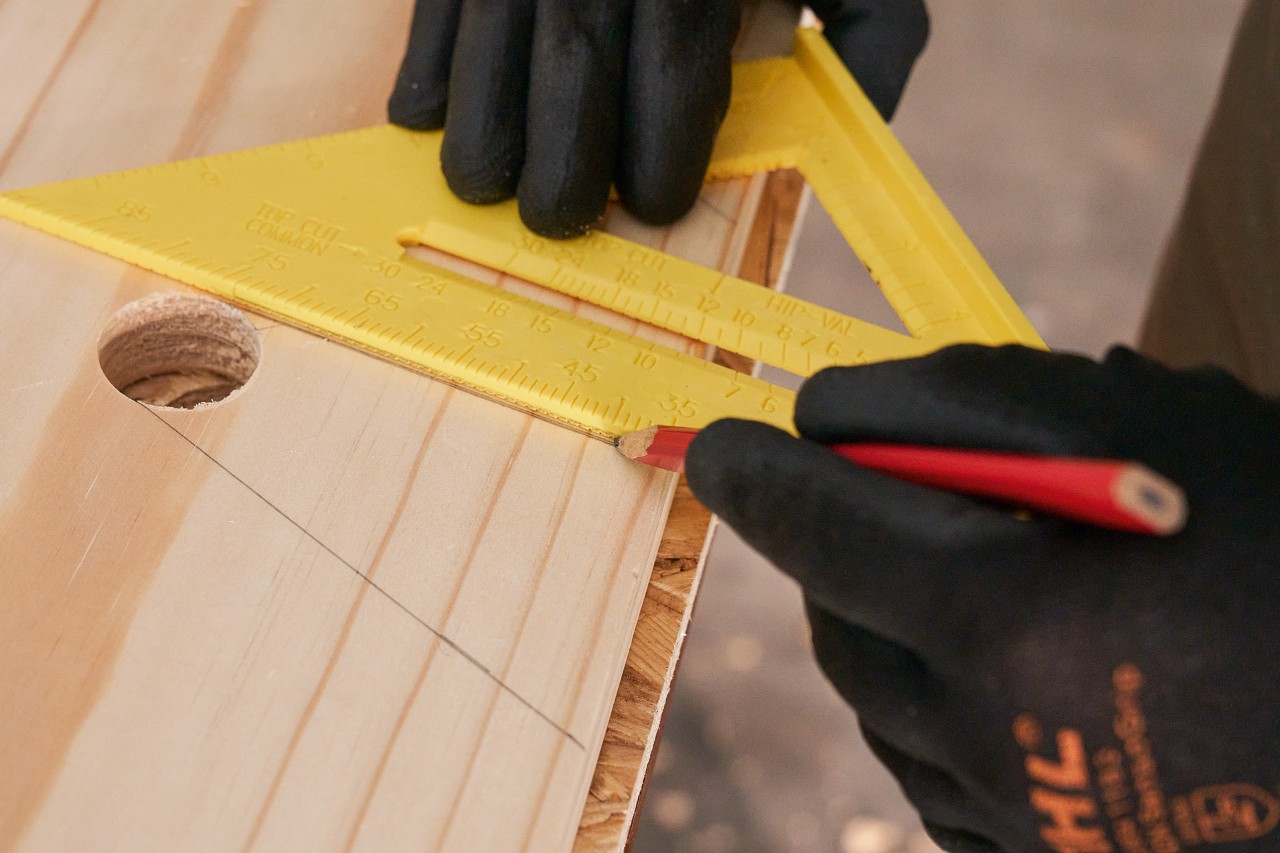 Alguien traza líneas en una tabla de madera con un lápiz y una escuadra para marcar las escotaduras. 