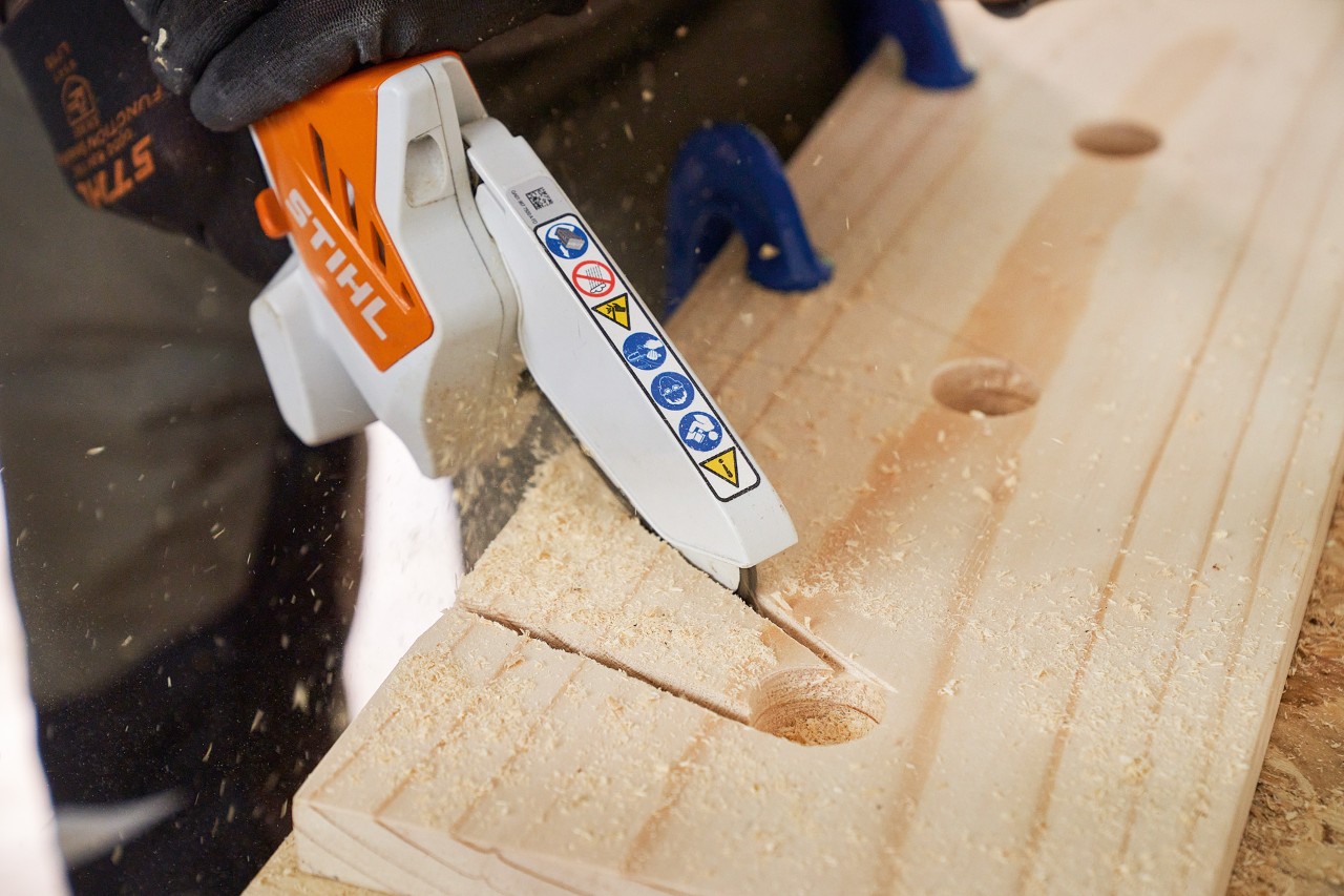 Una persona corta con la minisierra de batería STIHL GTA 26 escotaduras de una tabla de madera