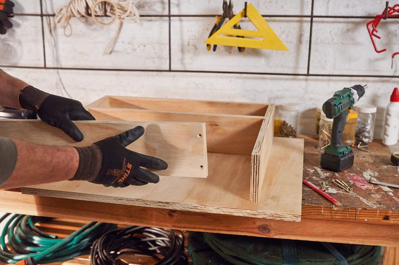 Un hombre construye cajones para guardar el cortacésped con tablas de madera 