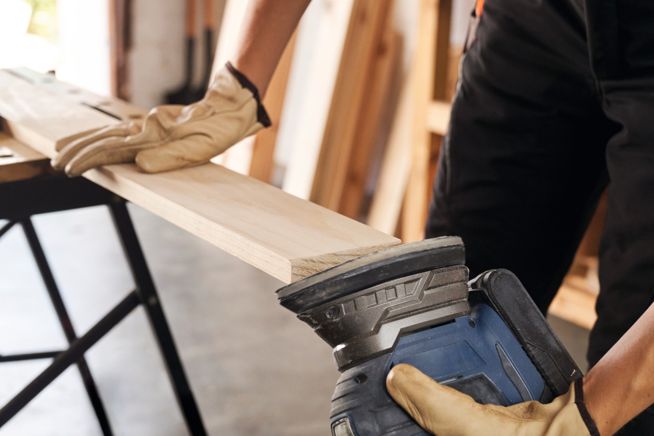 Primer plano de una mujer lijando piezas de madera con una rectificadora de batería