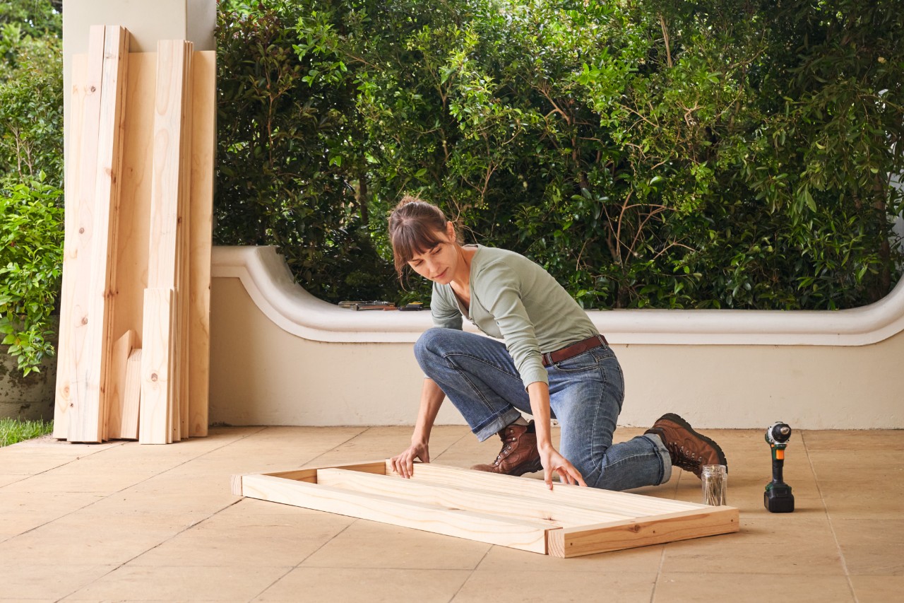 Una mujer coloca las piezas de madera para la estructura inferior del tejado en una terraza