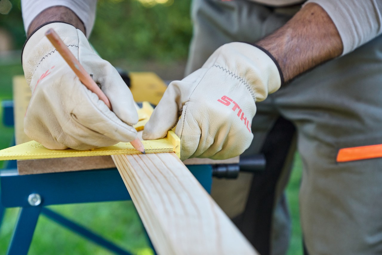 Primer plano de una persona dibujando marcas de longitud en listones de madera con una escuadra y un lápiz