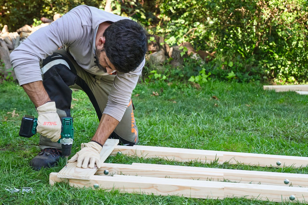 Un hombre atornilla una tabla a tres listones de madera para construir un caballete de madera