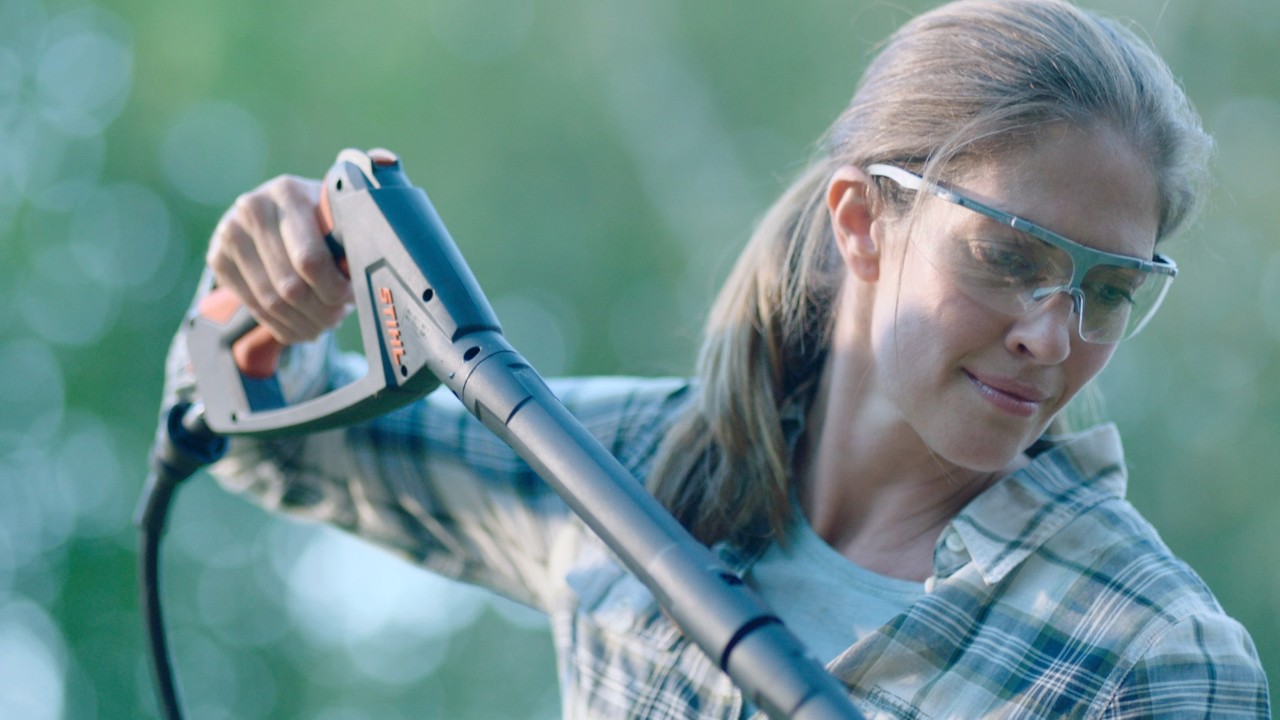 Una mujer con gafas de seguridad limpiando muebles de jardín de madera con una hidrolimpiadora STIHL RE 130 Plus.