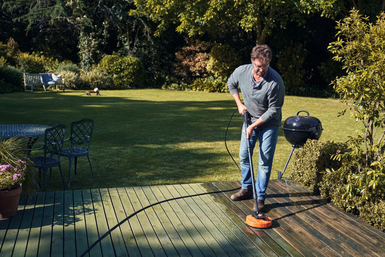 Un hombre limpia la terraza con un limpiador de superficies STIHL RA 82