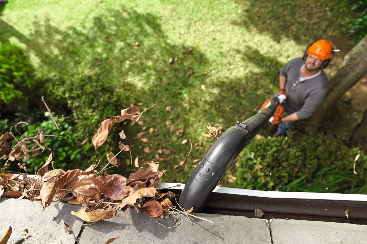 Un hombre limpia el canalón con el juego de limpieza de canalones STIHL