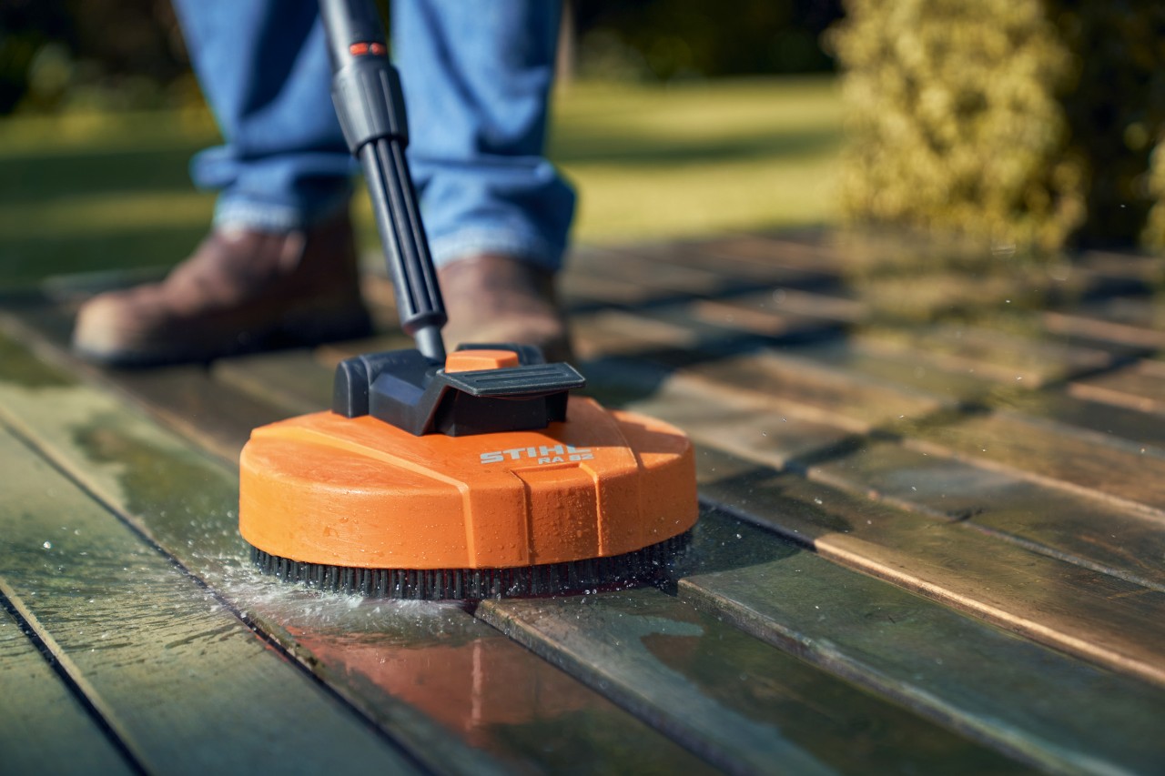 Primer plano del producto para limpiar el suelo de la terraza STIHL RA 82, limpiando los tablones de madera, dejante de los pies del usuario que la está utilizando