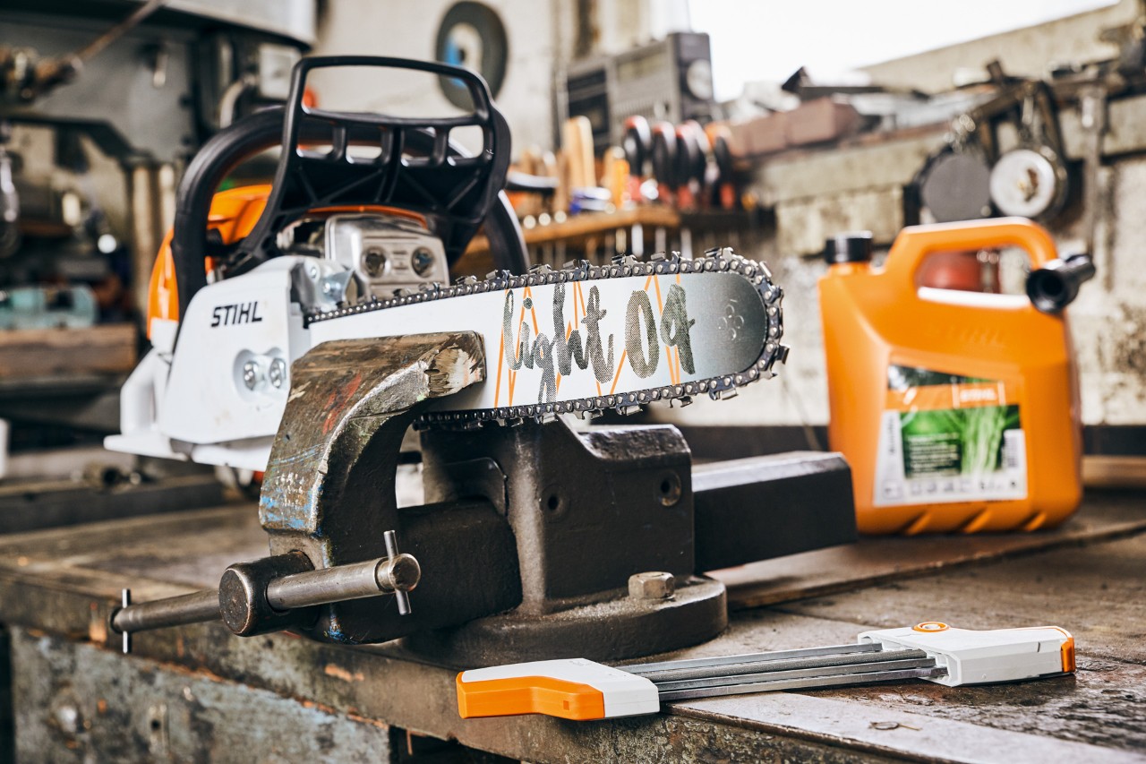 Una motosierra de gasolina STIHL MS 261 C-M con espada Light 04 sujeta a un banco de trabajo, con una botella de mezcla de combustible STIHL MotoMix detrás