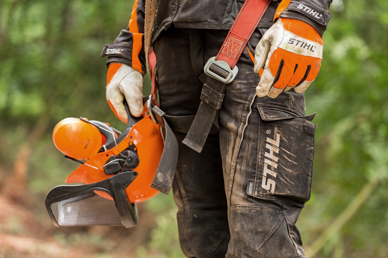 Una persona con ropa STIHL de protección: guantes de trabajo, pantalones con protección anticorte y casco