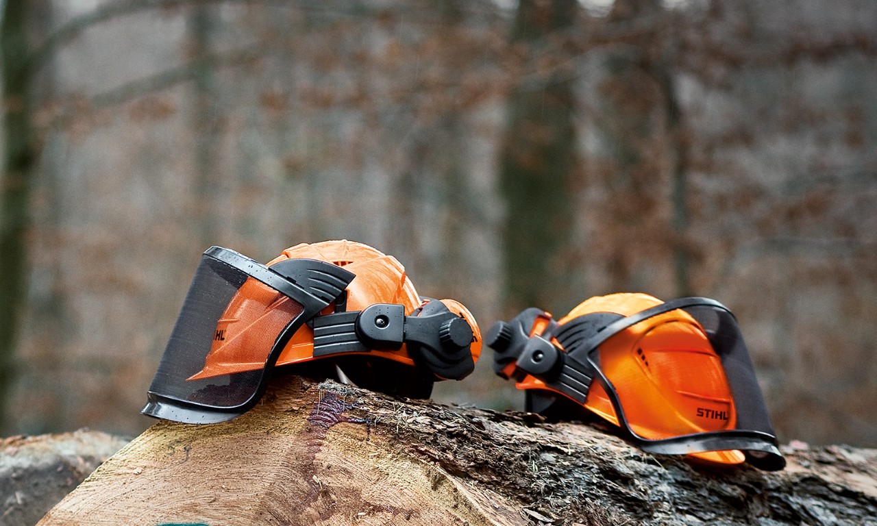 Ropa de protección para motosierras: dos cascos STIHL ADVANCE apoyados en troncos de árboles derribados en un bosque
