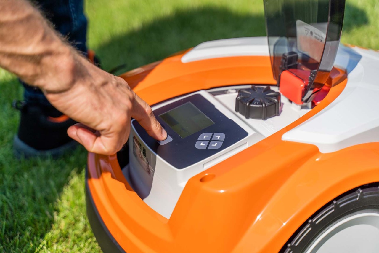El panel de control de un robot cortacésped STIHL iMOW® 422 y una persona pulsando uno de sus botones