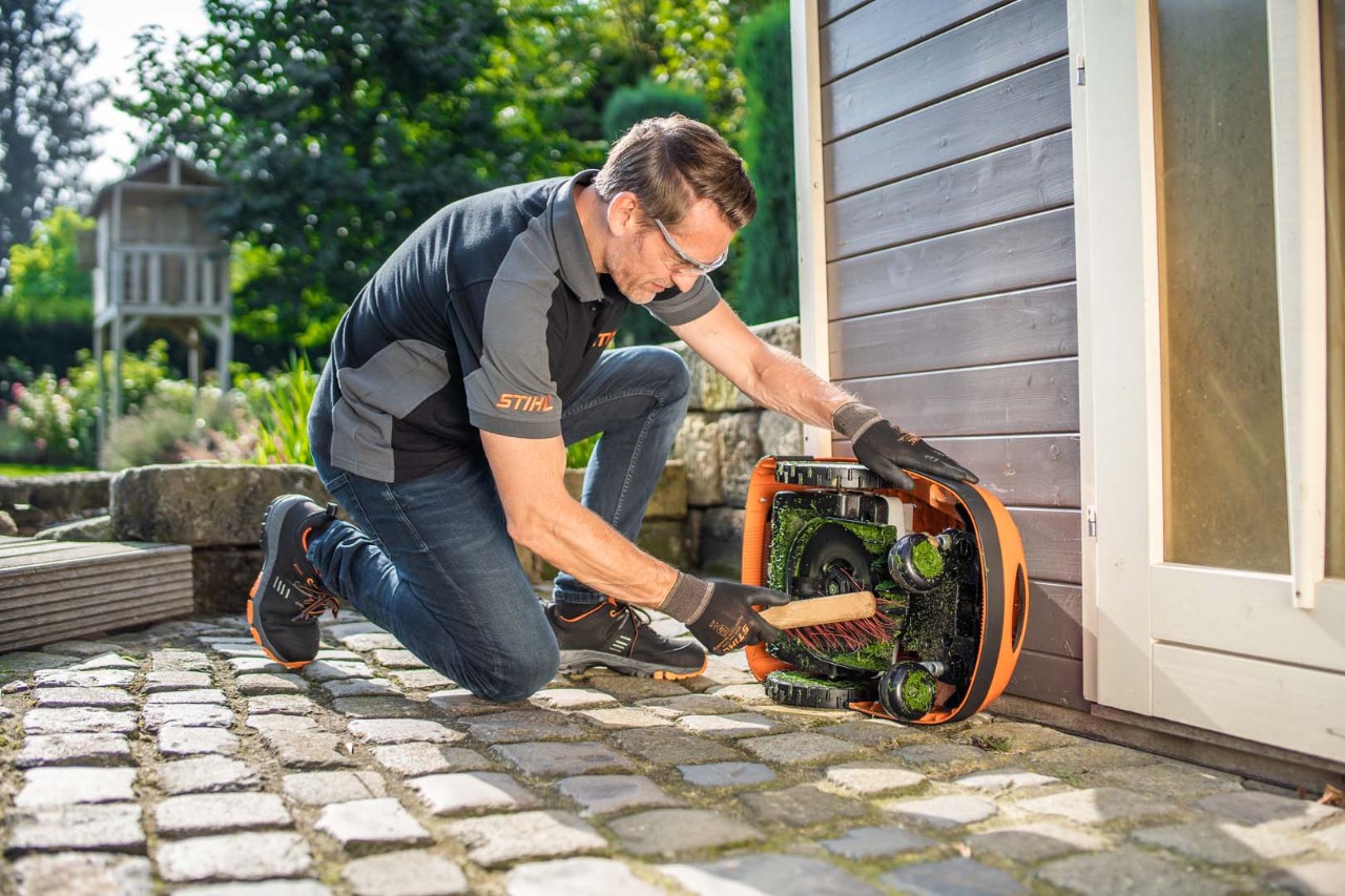 Un hombre utiliza un cepillo para limpiar la parte inferior de un robot cortacésped STIHL iMOW® 422