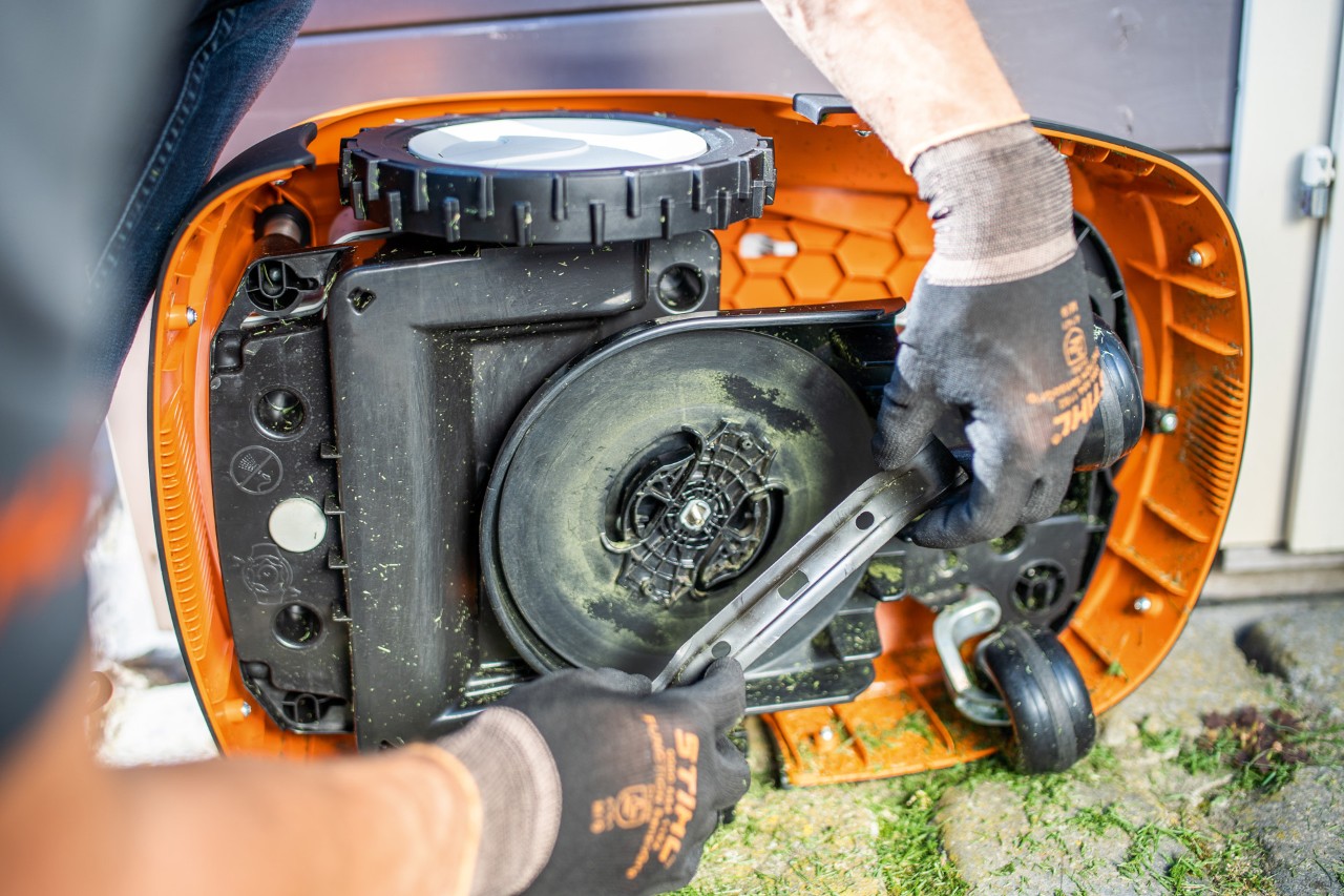 Una persona con guantes retira la cuchilla de corte de un robot cortacésped STIHL iMOW® 422