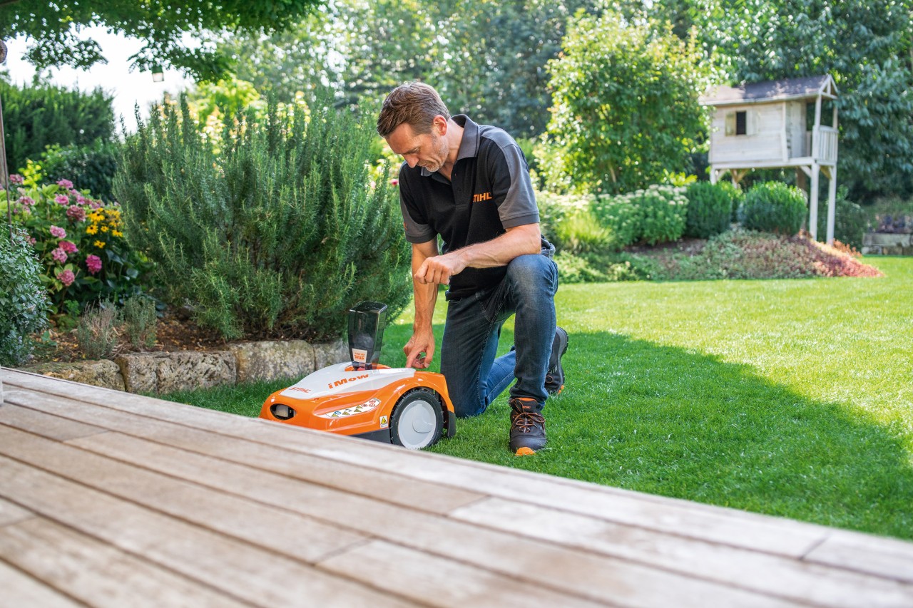 Un distribuidor STIHL utiliza el panel de control de un robot cortacésped STIHL iMOW® 422 en un jardín