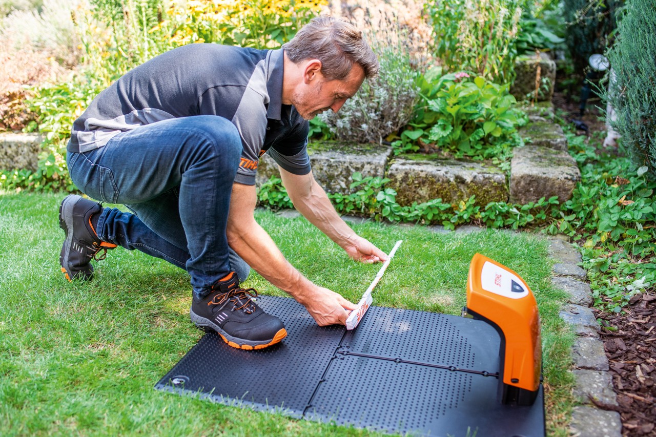 Un distribuidor STIHL instala la estación de carga de un robot cortacésped STIHL iMOW® 422 en un jardín