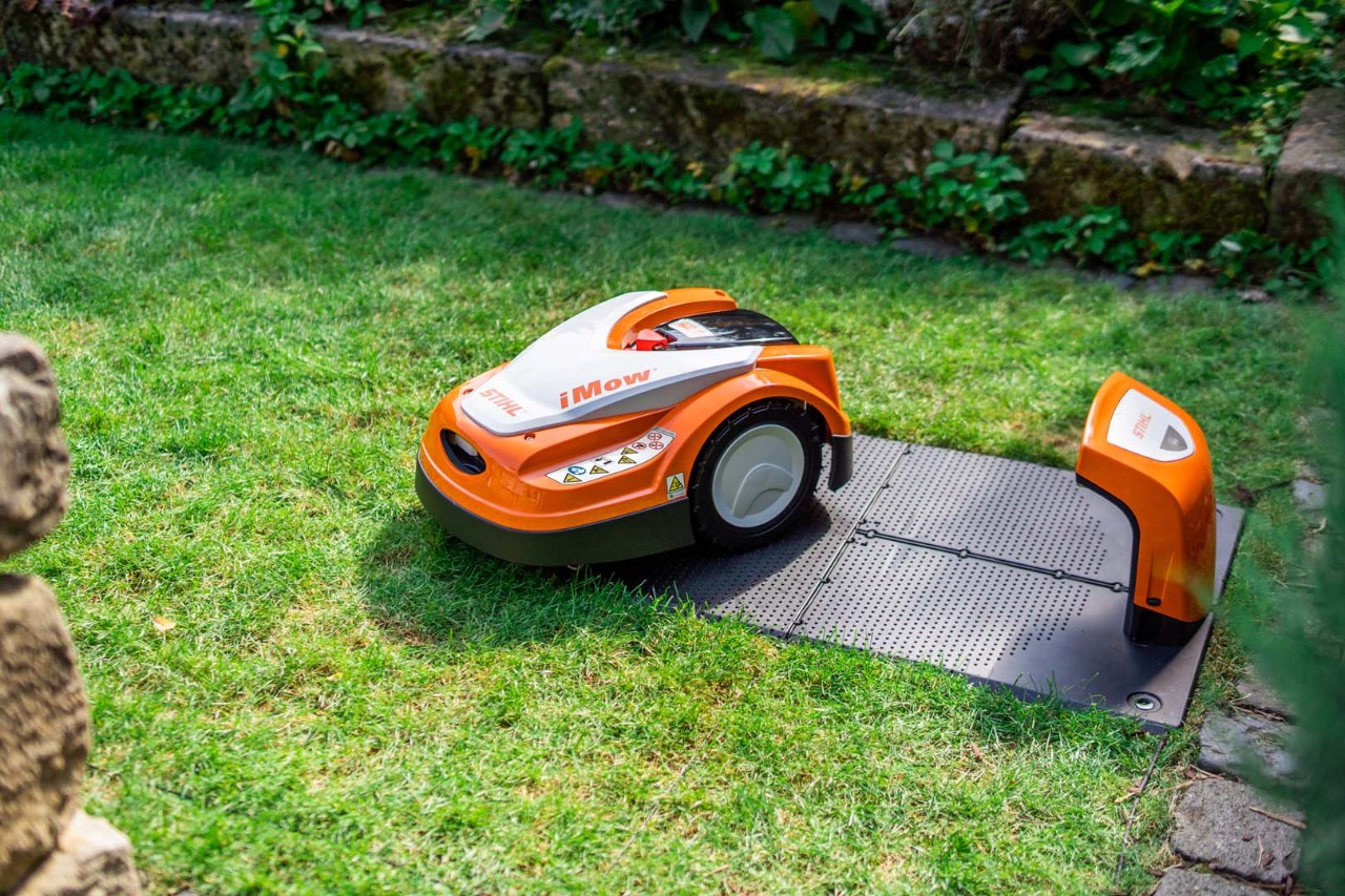 Un robot cortacésped STIHL iMOW® junto a su estación de carga sobre césped verde 