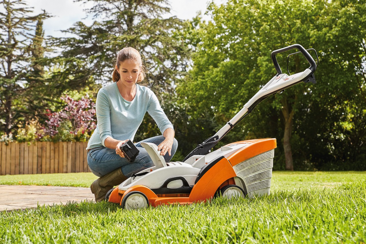 Una mujer arrodillada junto a un cortacésped STIHL RMA 339 C retirando la batería