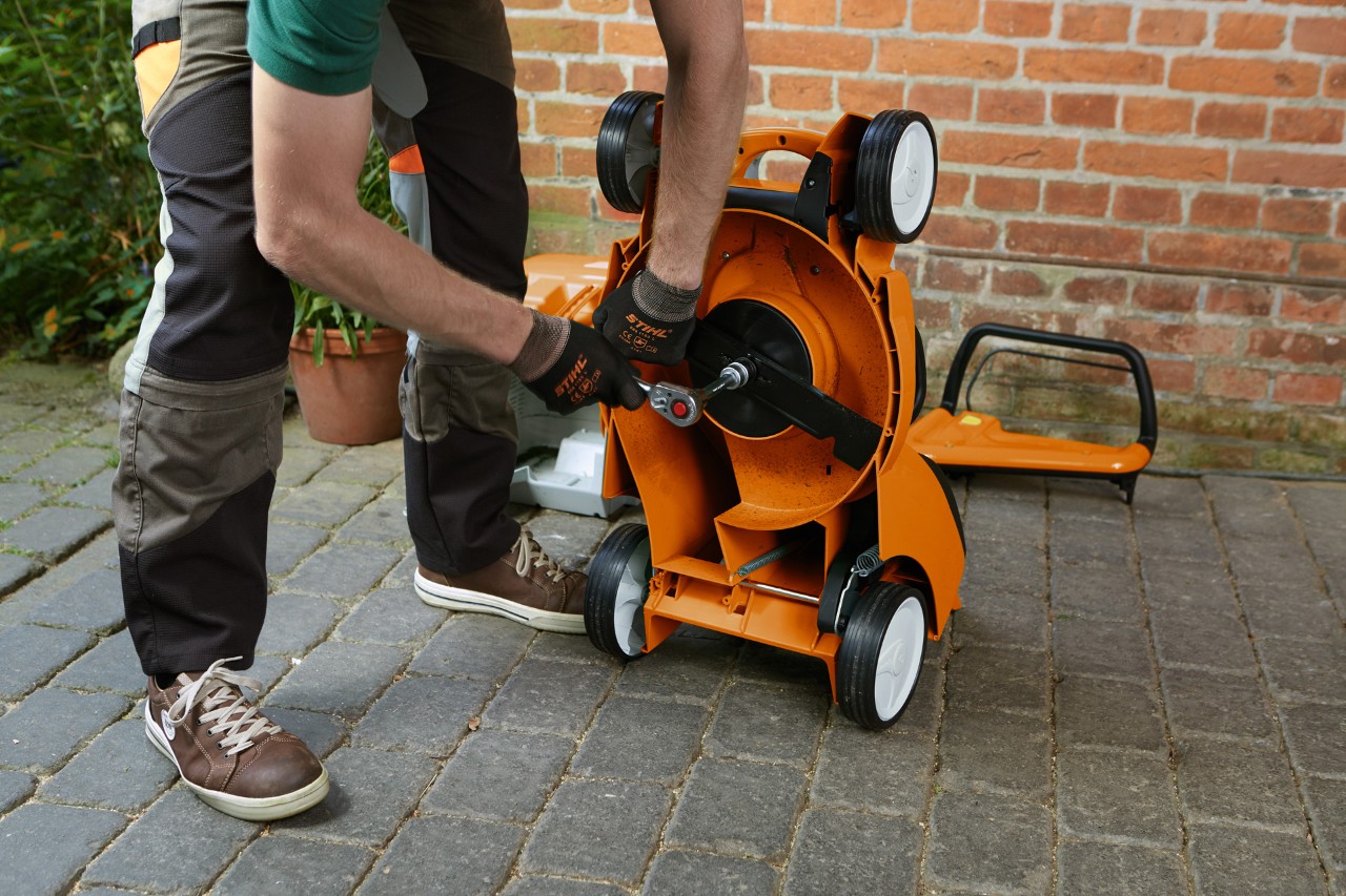 Una persona con guantes retira la cuchilla de un cortacésped STIHL RM inclinado