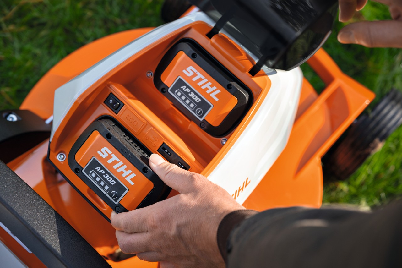 Una persona coloca la batería STIHL AP 300 completamente cargada en un cortacésped
