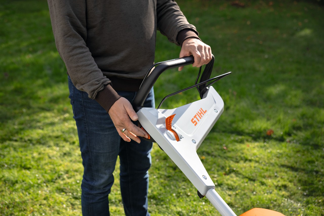 Una persona en un prado presiona el botón de arranque de un cortacésped de batería STIHL