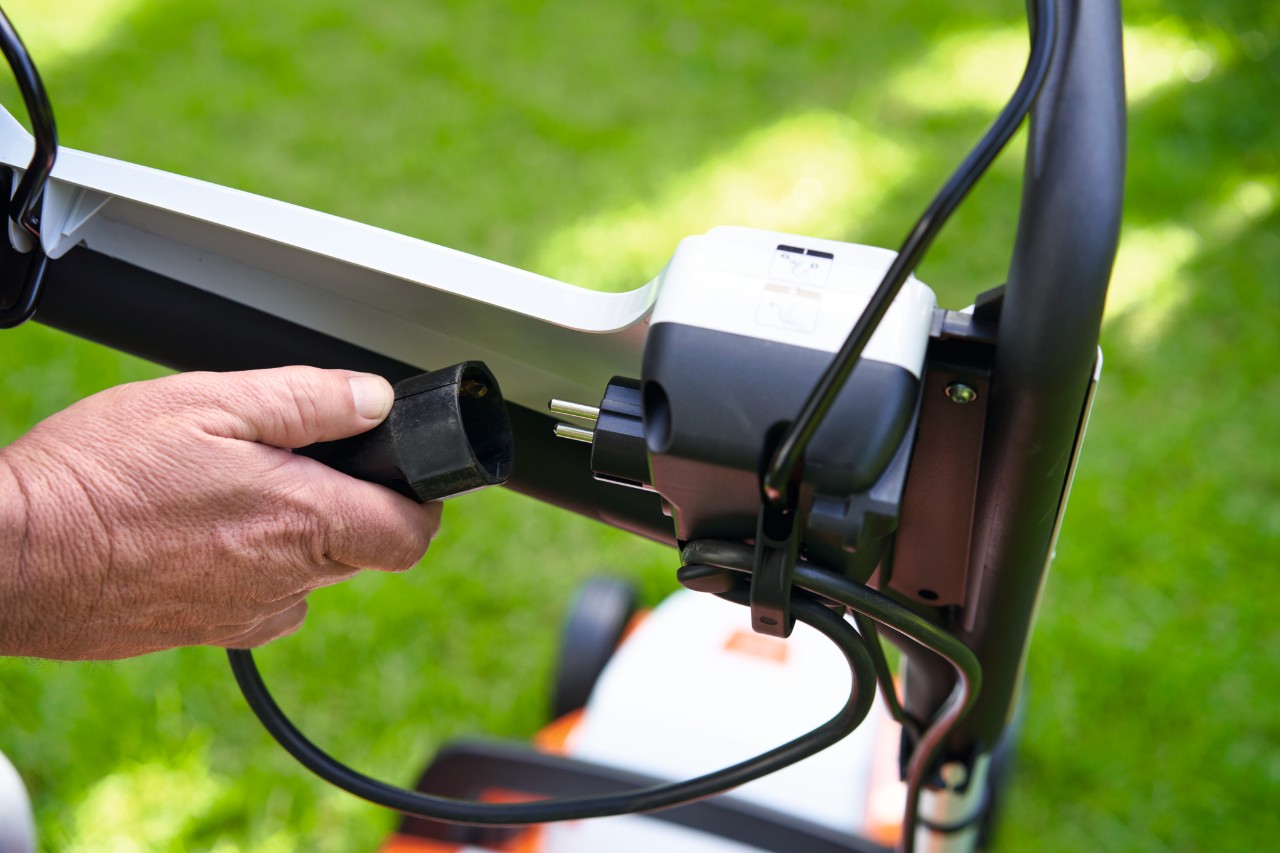 Una persona conecta el cable de alimentación al cortacésped