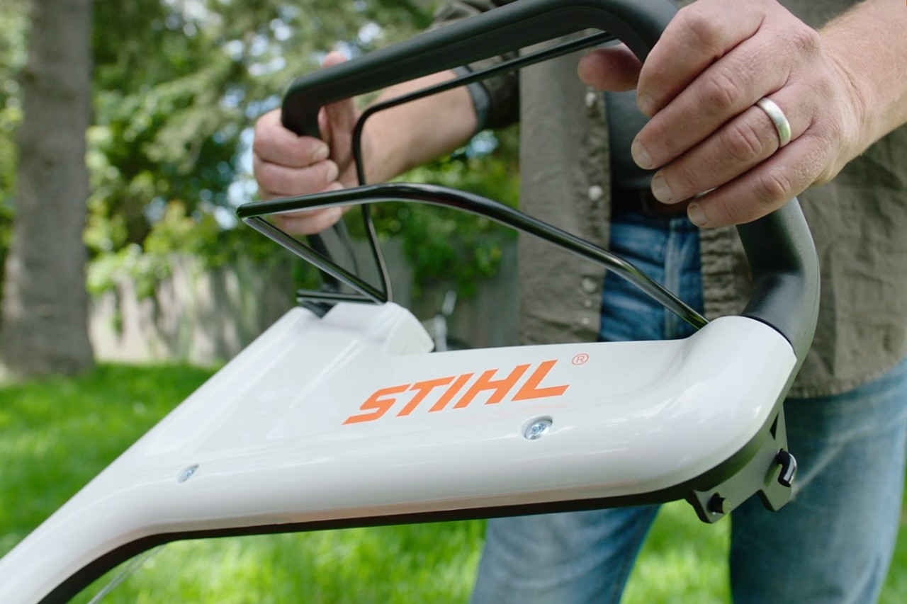 Una persona presiona la palanca de parada del motor de un cortacésped STIHL
