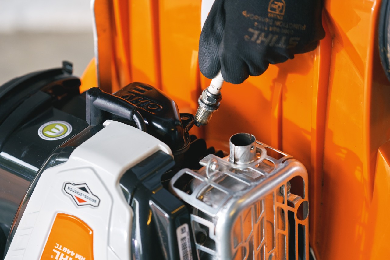 Desconexión de la bujía de un cortacésped de gasolina STIHL RM 448 T-C antes de limpiar el carburador del cortacésped. Image source: RM-RM448TC-AW-052