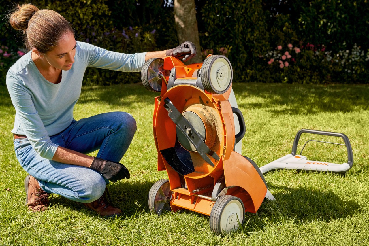 Una mujer mira con detenimiento tras limpiar un cortacésped de batería STIHL RMA 339C en un jardín.