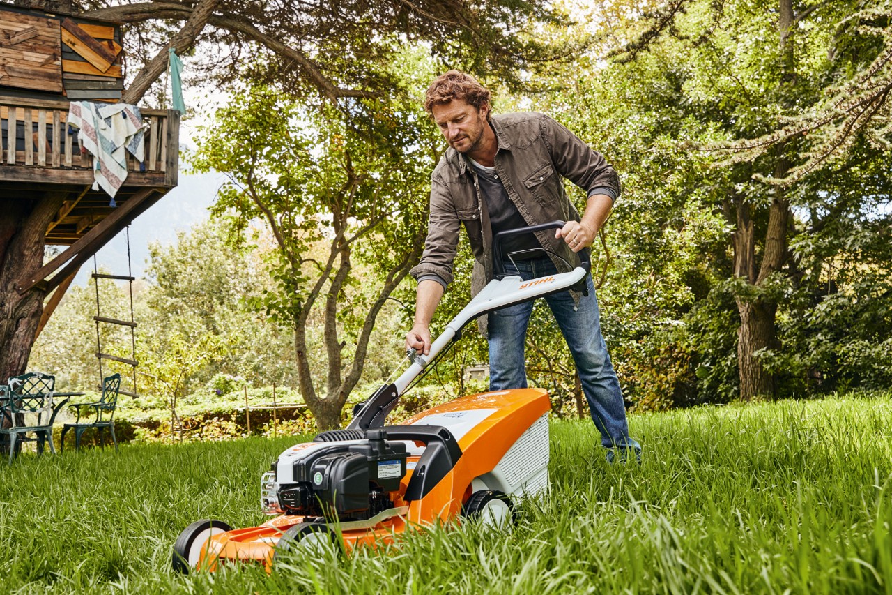 Un hombre en una parcela de jardín corta el césped con un cortacésped STIHL con motor STIHL 4-Mix®