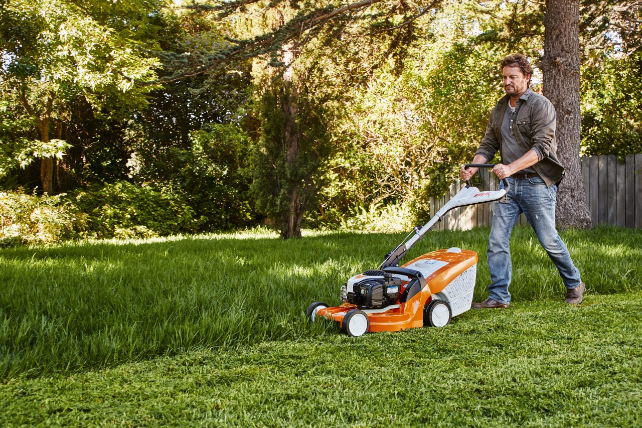Un hombre corta el césped en un jardín con un cortacésped STIHL. 