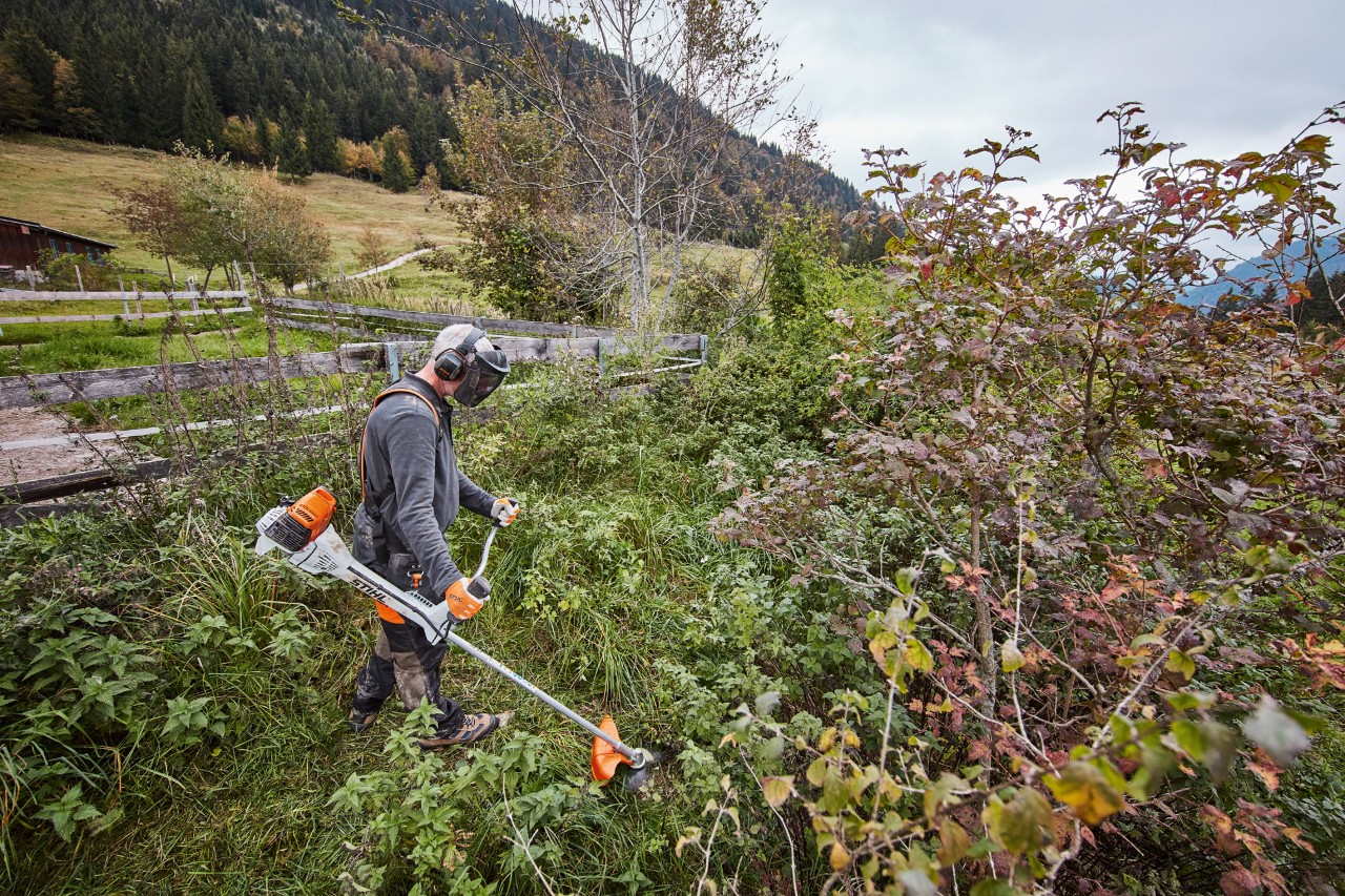 Un hombre con equipamiento de protección individual corta matorrales con una desbrozadora de gasolina STIHL FS 311