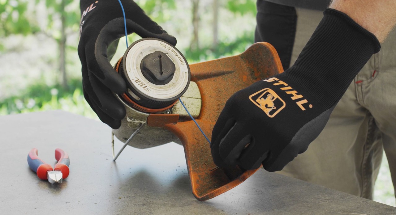 Primer plano de una persona enrollando un hilo de corte en un cortabordes de batería STIHL FSA 57