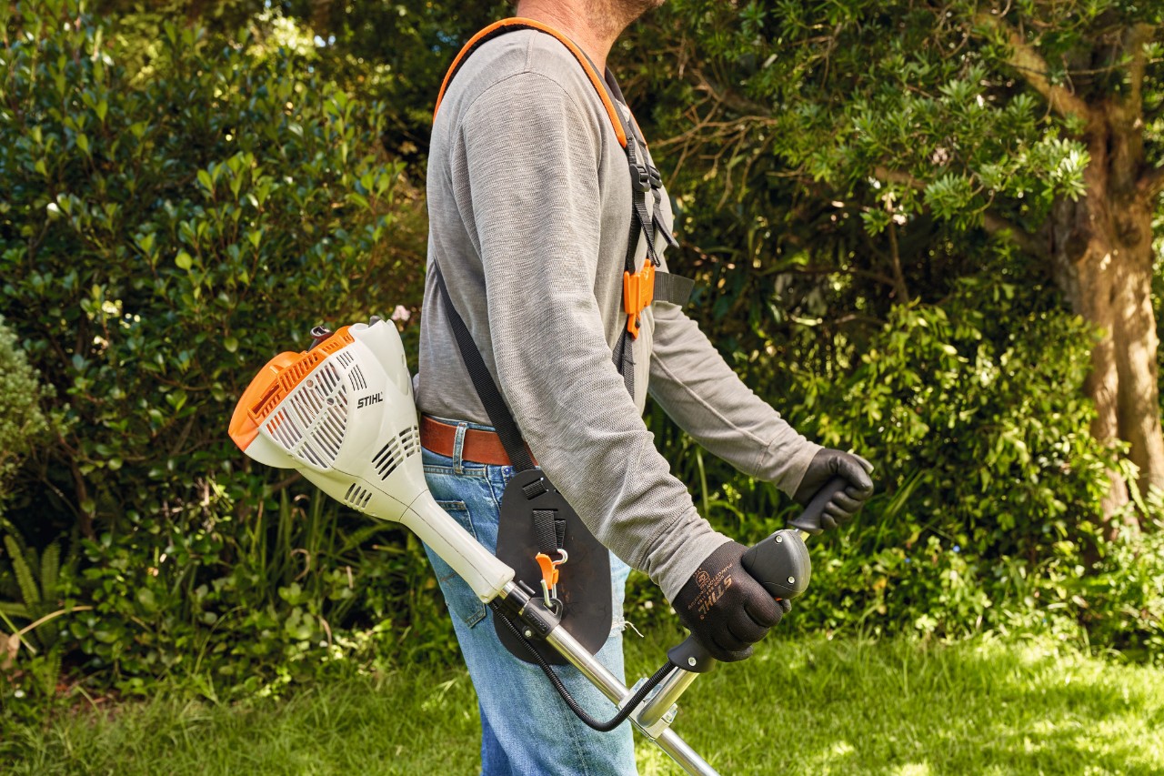 Un hombre levanta la desbrozadora de gasolina STIHL FS 91 del suelo para empezar a segar