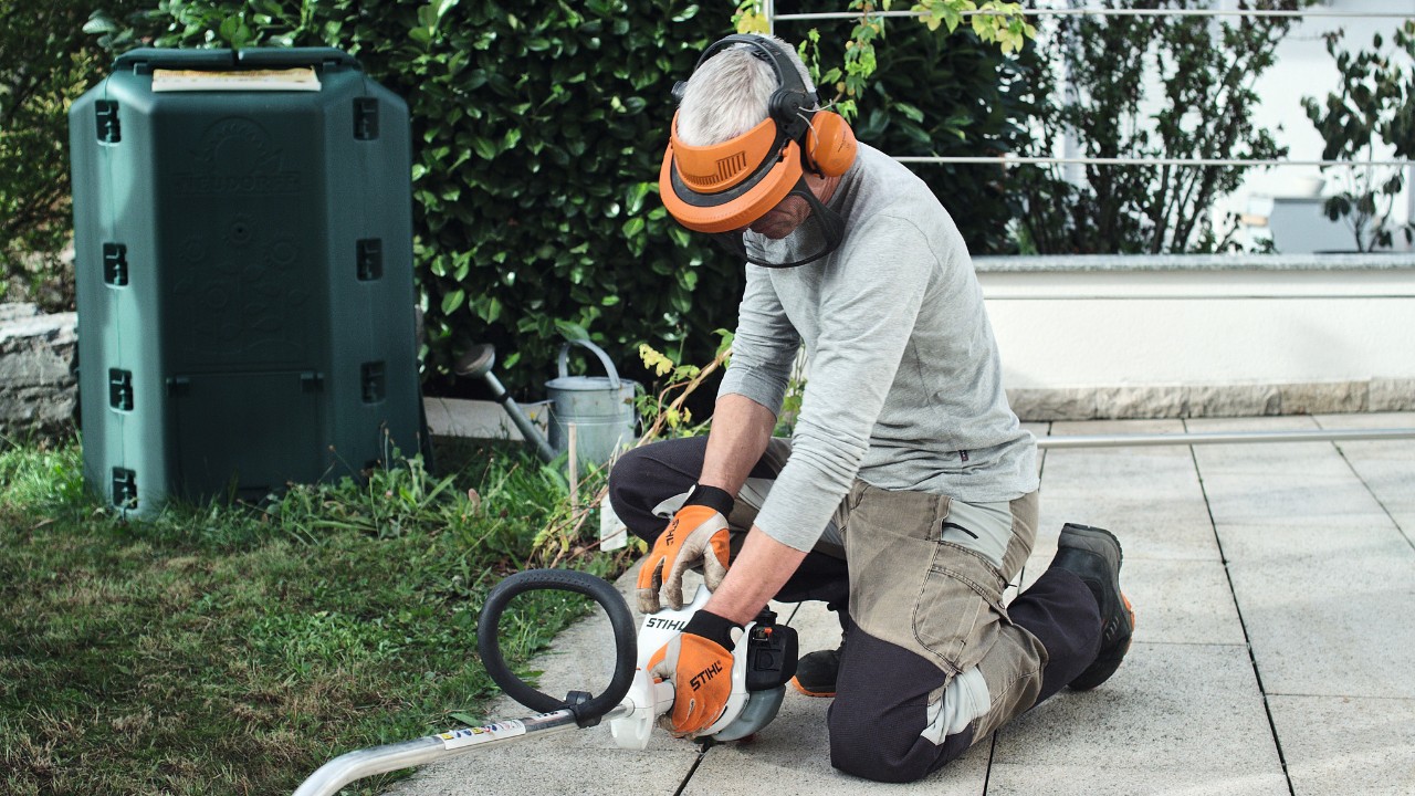 La desbrozadora de gasolina STIHL FS 38 es presionada contra el suelo por una persona con ropa de protección