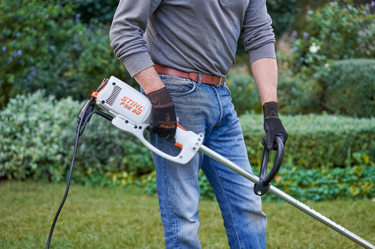 Hombre con guantes de protección agarra con ambas manos la desbrozadora eléctrica STIHL FSE 60