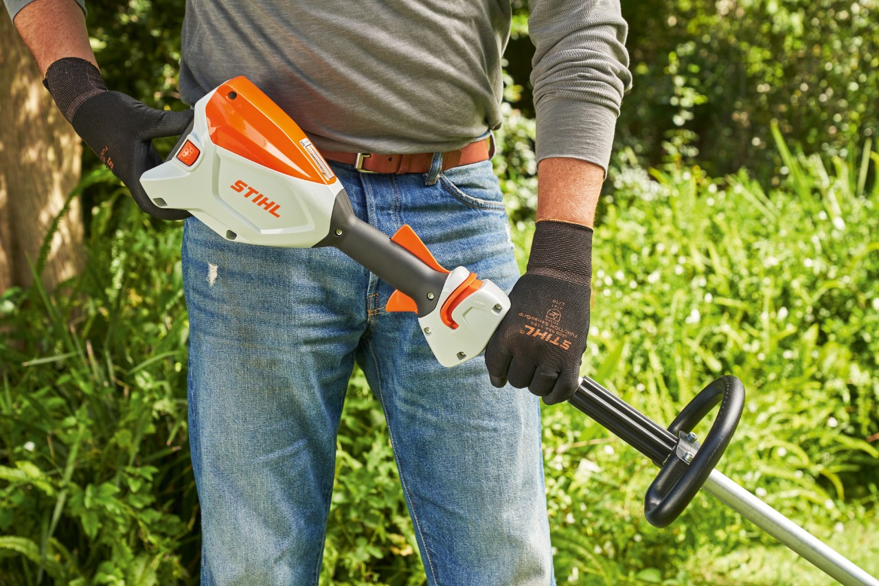 Hombre con guantes de protección comprueba la batería de la desbrozadora sin cable STIHL FSA 60 para ponerla en marcha