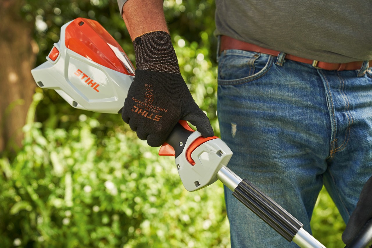 Un hombre con guantes de protección empuja la corredera de desbloqueo de la desbrozadora sin cable STIHL FSA 60 hacia el mango integral