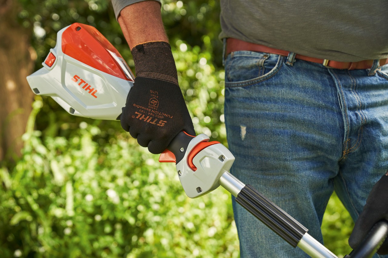 Hombre con guantes de protección presiona el bloqueo de la palanca de control de la desbrozadora sin cable STIHL FSA 60