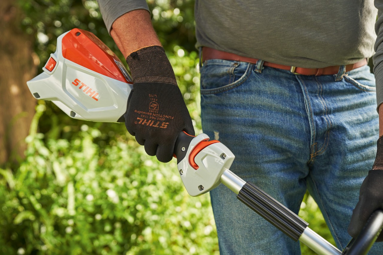 Hombre con guantes de protección acciona la palanca de control de la desbrozadora sin cable STIHL FSA 60 para ponerla en marcha