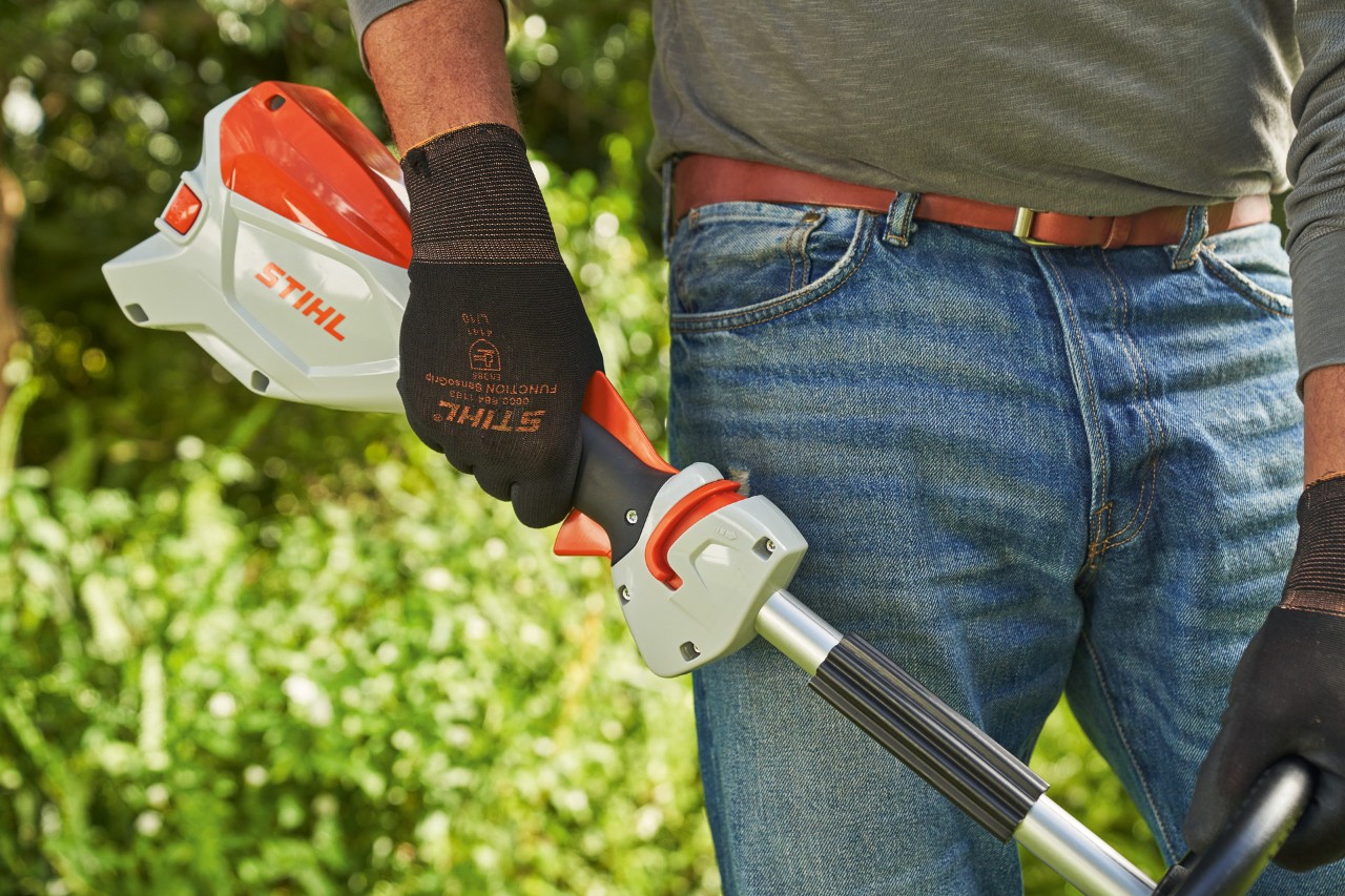 Un hombre con guantes de protección suelta la palanca de control de la desbrozadora sin cable STIHL FSA 60 para apagarla