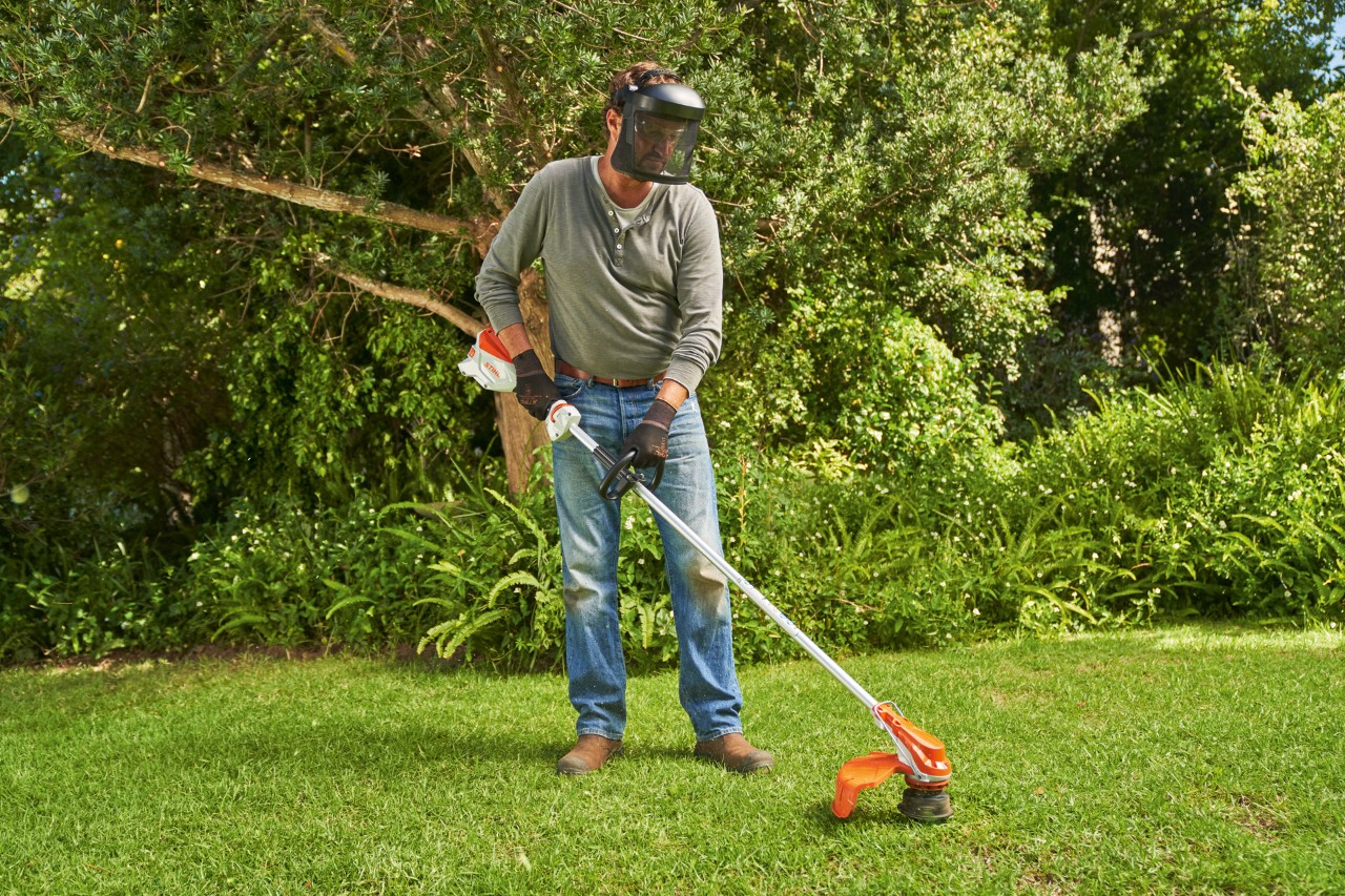 Un hombre con careta corta el césped de un jardín con la desbrozadora inalámbrica STIHL FSA 60
